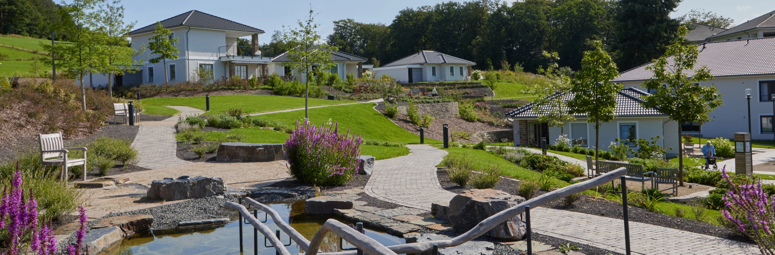 Moderne Wohnanlage mit gepflegter Parklandschaft, barrierefreien Wegen, Wasseranlage und hochwertiger Architektur. Helle Einfamilienhäuser in naturnaher Umgebung mit großzügigen Grünflächen, Sitzbereichen und liebevoll gestalteter Gartenanlage – ideal für komfortables Wohnen, Seniorenresidenz, betreutes Wohnen oder exklusives Wohnquartier im Grünen